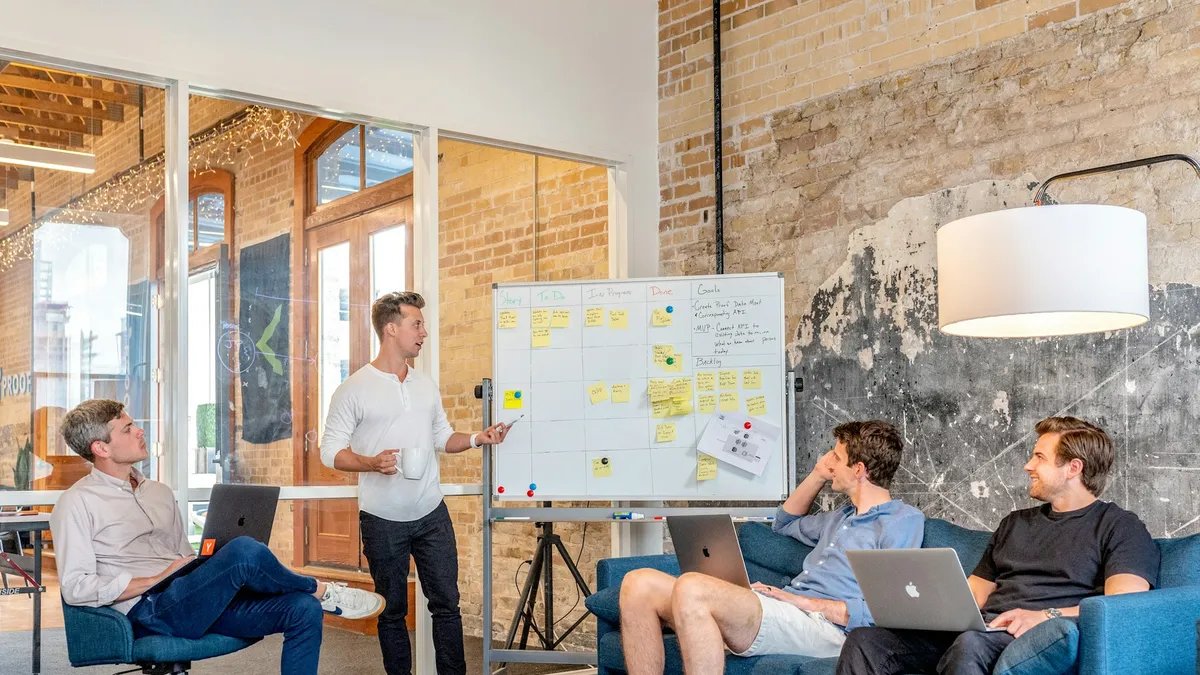 Startup founder presenting a plan on a whiteboard to his early team in a bright office
